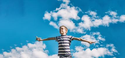 Boy holding an airplane flying it with blue sky and clouds behind him