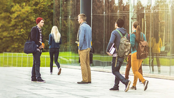 2 students are talking on the street near a transparent building, while others are walking somewhere