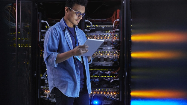 Focused male IT technician using digital tablet at panel in dark server room