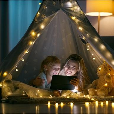 mother and daughter watching tablet in lit up tent