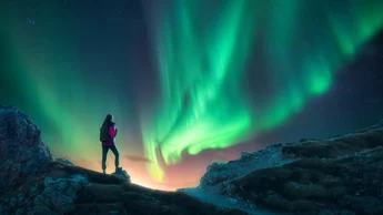 Northern lights and young woman on mountain peak at night