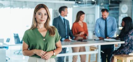 woman smiling at camera while group works at table behind her