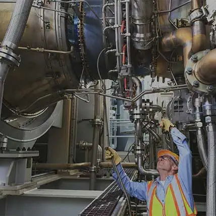 Engineer examining instrumentation cables at fuel injection stage of gas turbine which drives generators in power plant while turbine is powered down