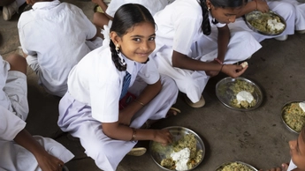 young girl in school uniform eating a meal among classmates