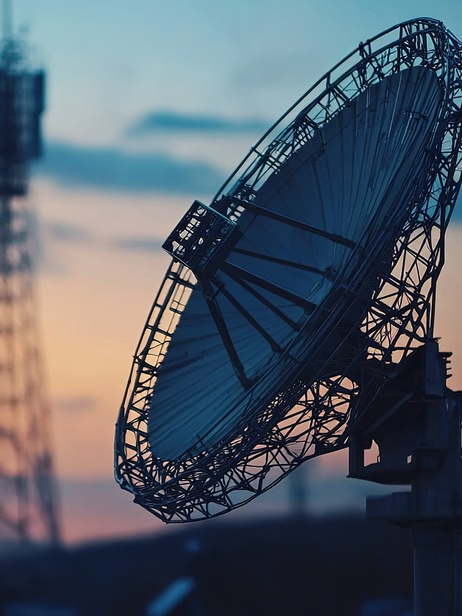 A silhouette of a large satellite dish against a sunset, framed by telecommunications towers, showcasing the blend of technology and nature.