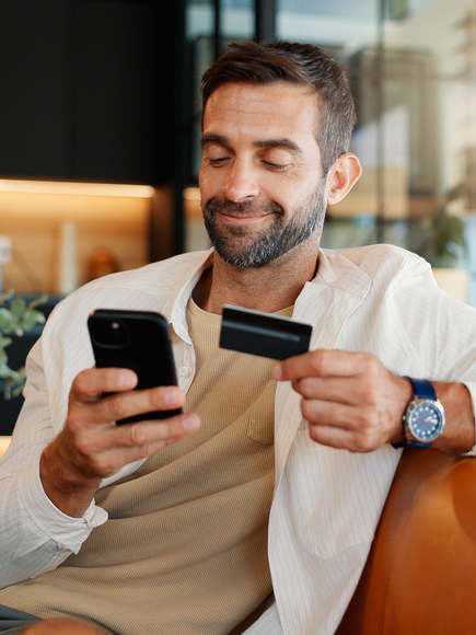 Credit card, mobile and happy man with payment in home for online shopping, internet banking or purchase. Phone, debit and person with digital money in living room for ecommerce, finance or deposit