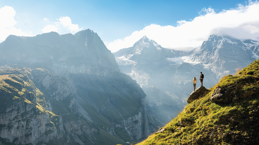 An adventurous man stands on top of a mountain and enjoys a beautiful view during sunny summer day,  Beautiful nature with steep mountains and rocks in background. Swiss Alps. Discover