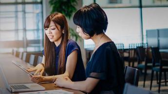 two women working together at a counter with laptop