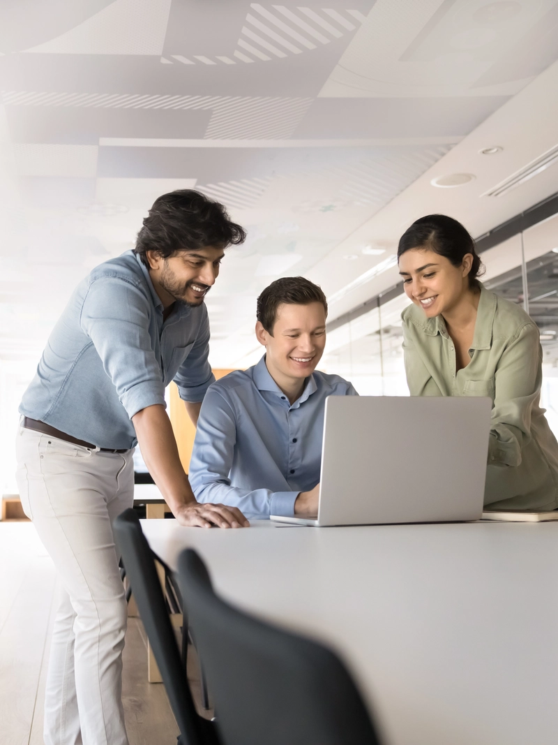 Three colleagues gathered around laptop in modern coworking space