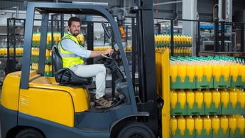 Factory worker loading packed juice bottles on forklift in factory 