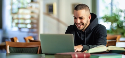 Male student using notebook and books and learning in the university library