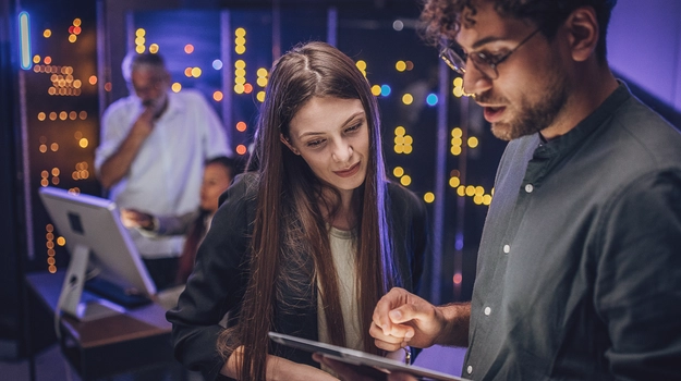 Engineers examining data on digital tablet together in server room.
