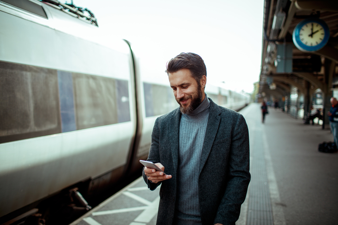 Young man using a smart phone while waiting for his train at the train station