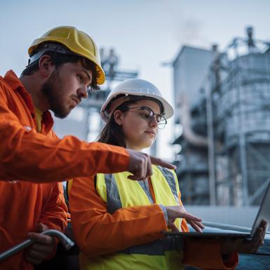 two workers in hard hats working over a laptop