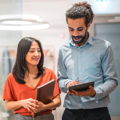 two colleagues walking down a hall reviewing tablet