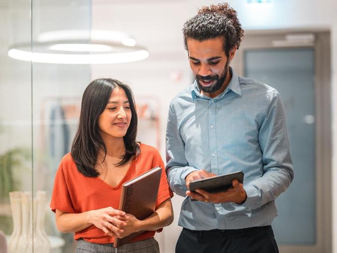 two colleagues walking down a hall reviewing tablet