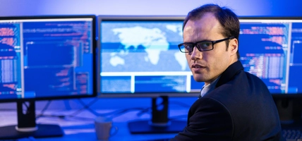 man at desk with multiple screens looking at camera