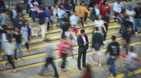 High angle view of businessman using smart phone amidst crowd. Professional is standing on busy street. He is surrounded by people in city.