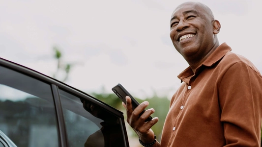 man smiling while next to car holding mobile phone